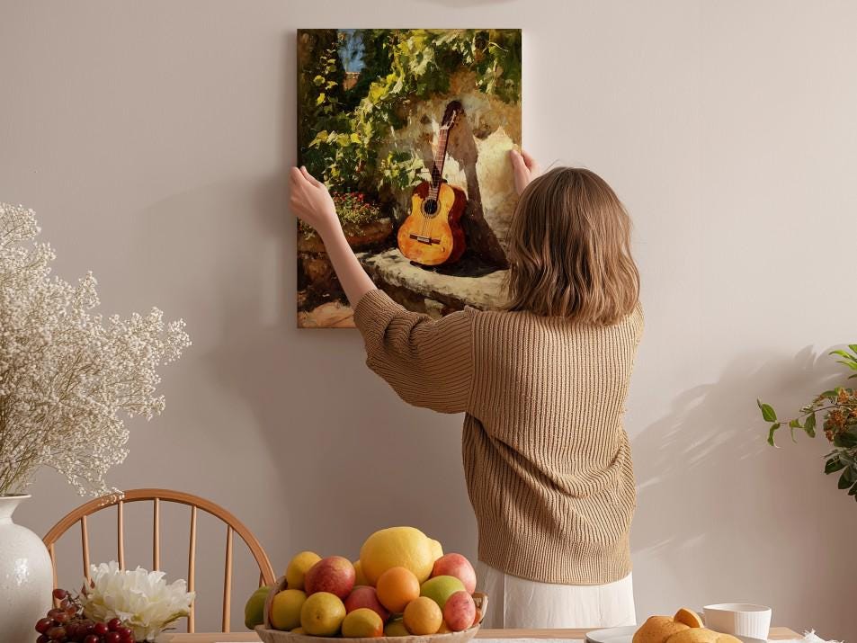 A woman hangs a framed painting of a guitar on a wall in a cozy room with a dining table, chairs, and various fruits.