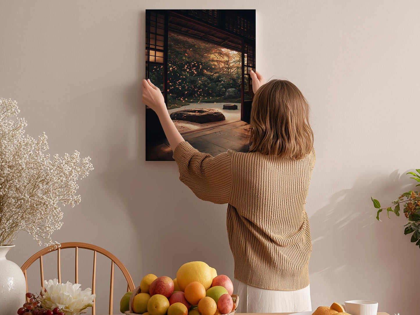 A woman hangs a framed picture on a wall in a cozy, homely setting with a dining table, chairs, and various decorative elements.