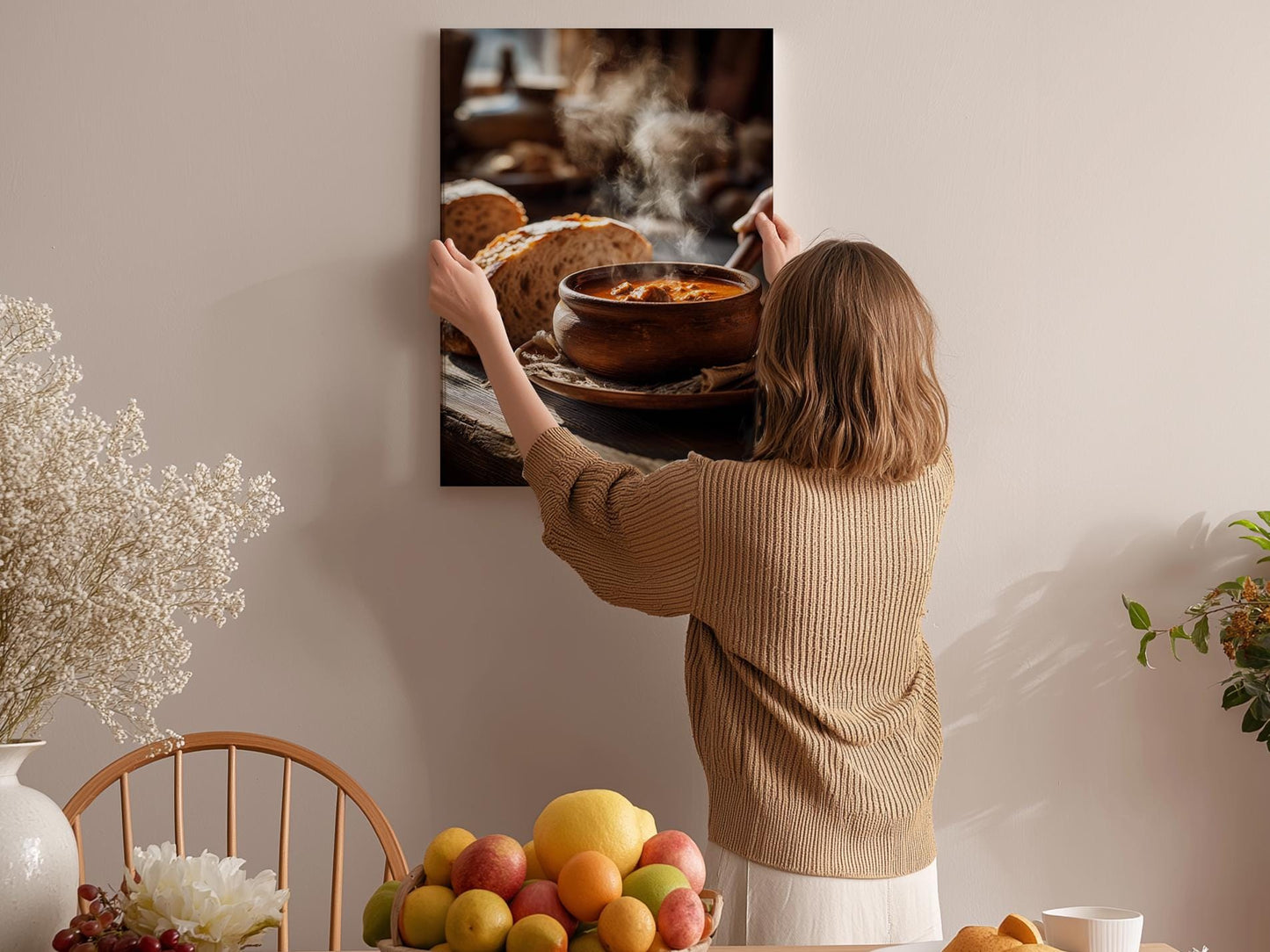 A woman hangs a framed photograph of a bowl of soup on a wall in a cozy kitchen setting.