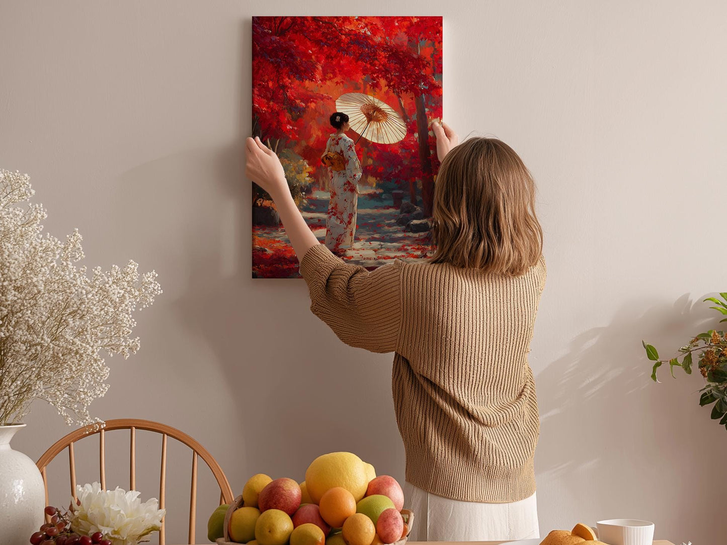 A woman hangs a vibrant painting of a woman in a red kimono holding an umbrella on a wall in a cozy room with a dining table and various fruits.