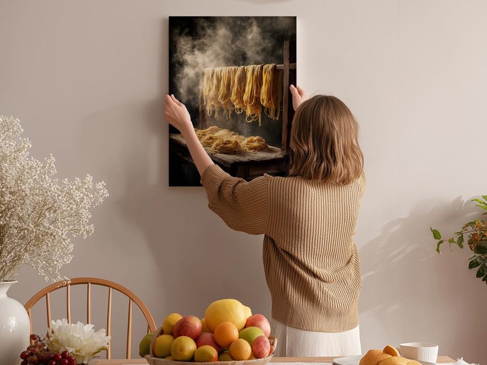 A woman hangs a framed photograph of noodles on a wall in a cozy kitchen setting.