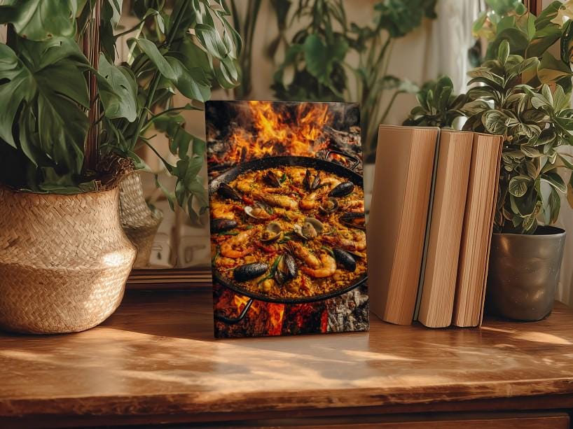 a framed photograph of a paella dish, surrounded by potted plants and books on a wooden surface.