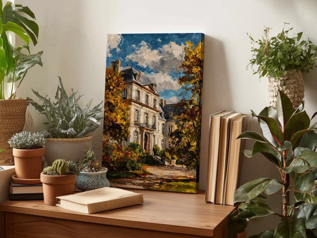 a painting of a house surrounded by trees, placed on a wooden surface next to several potted plants and books.