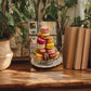 a wooden table with a framed painting of colorful macarons, surrounded by potted plants and books.