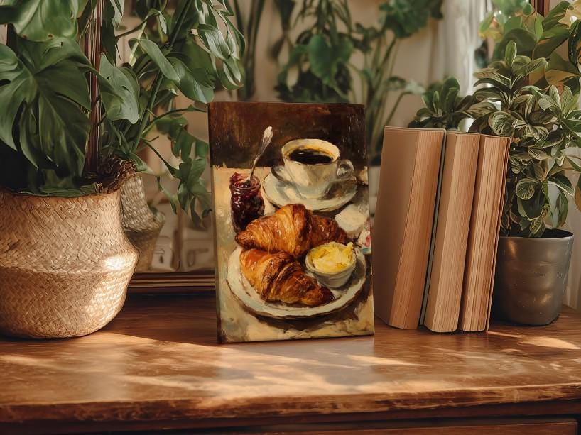 A painting of a croissant and coffee is displayed on a wooden table, surrounded by potted plants and books.