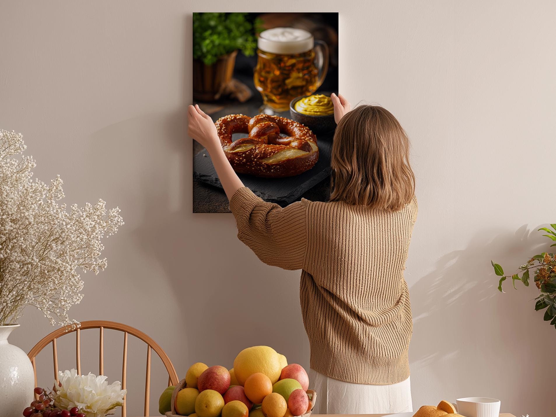 A woman hangs a framed photograph of a pretzel and a mug of beer on a wall in a cozy kitchen setting.