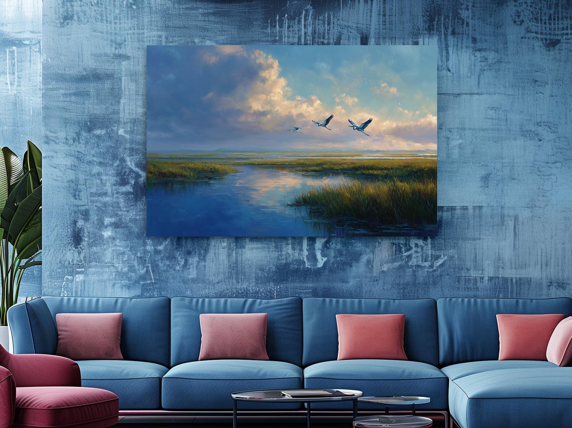 a large blue sofa with red throw pillows, positioned in front of a wall with a painting depicting a serene landscape with two birds flying over a body of water.