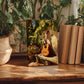a wooden table with a framed painting of a guitar, surrounded by potted plants and books, creating a cozy and artistic atmosphere.