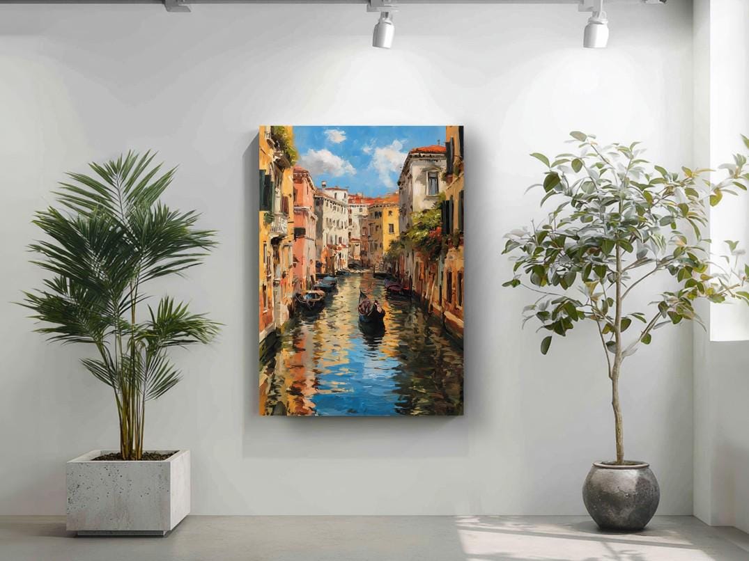 a painting of a canal in Venice, Italy, with colorful buildings lining the waterway and a gondola visible in the distance. The painting is hung on a white wall, and there are two potted plants in the foreground, one on the left and one on the right.