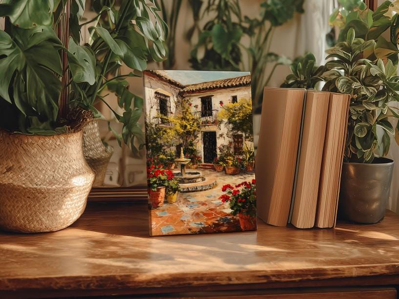 a wooden table with a framed painting of a courtyard scene, surrounded by potted plants and books.