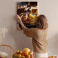 A woman hangs a framed photograph of a plate of food on a wall in a cozy kitchen setting.
