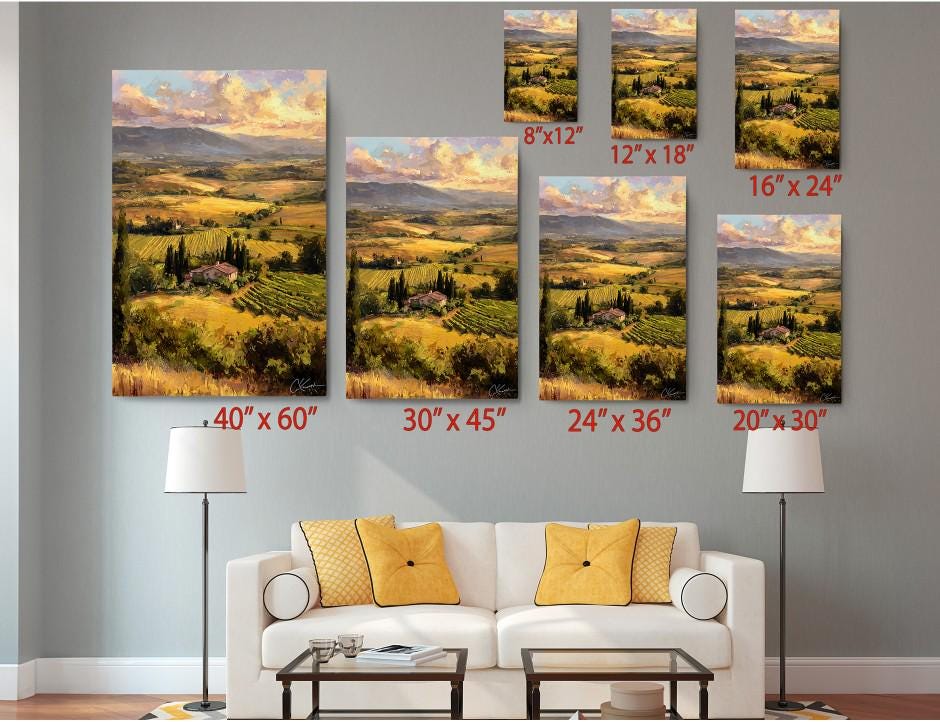 The image is a living room with a white sofa and a coffee table. Above the sofa, there are six framed landscape paintings of varying sizes, each depicting a different countryside scene. The paintings are arranged in a grid-like pattern on the wall, with each one showing a different perspective of the countryside landscape.