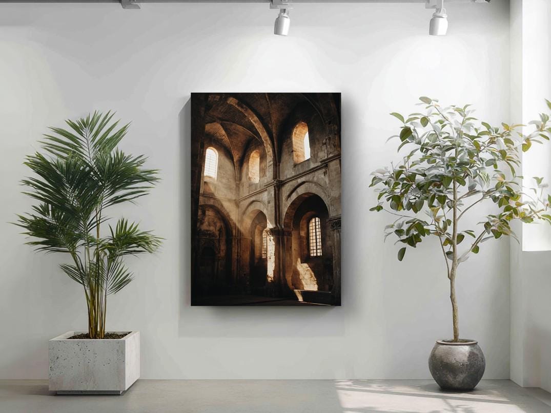 a large framed picture of a church with arched windows, hanging on a white wall between two potted plants.