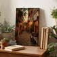 a cozy indoor setting with a wooden table displaying various items, including a framed photograph of a cobblestone street, potted plants, books, and a motorcycle.