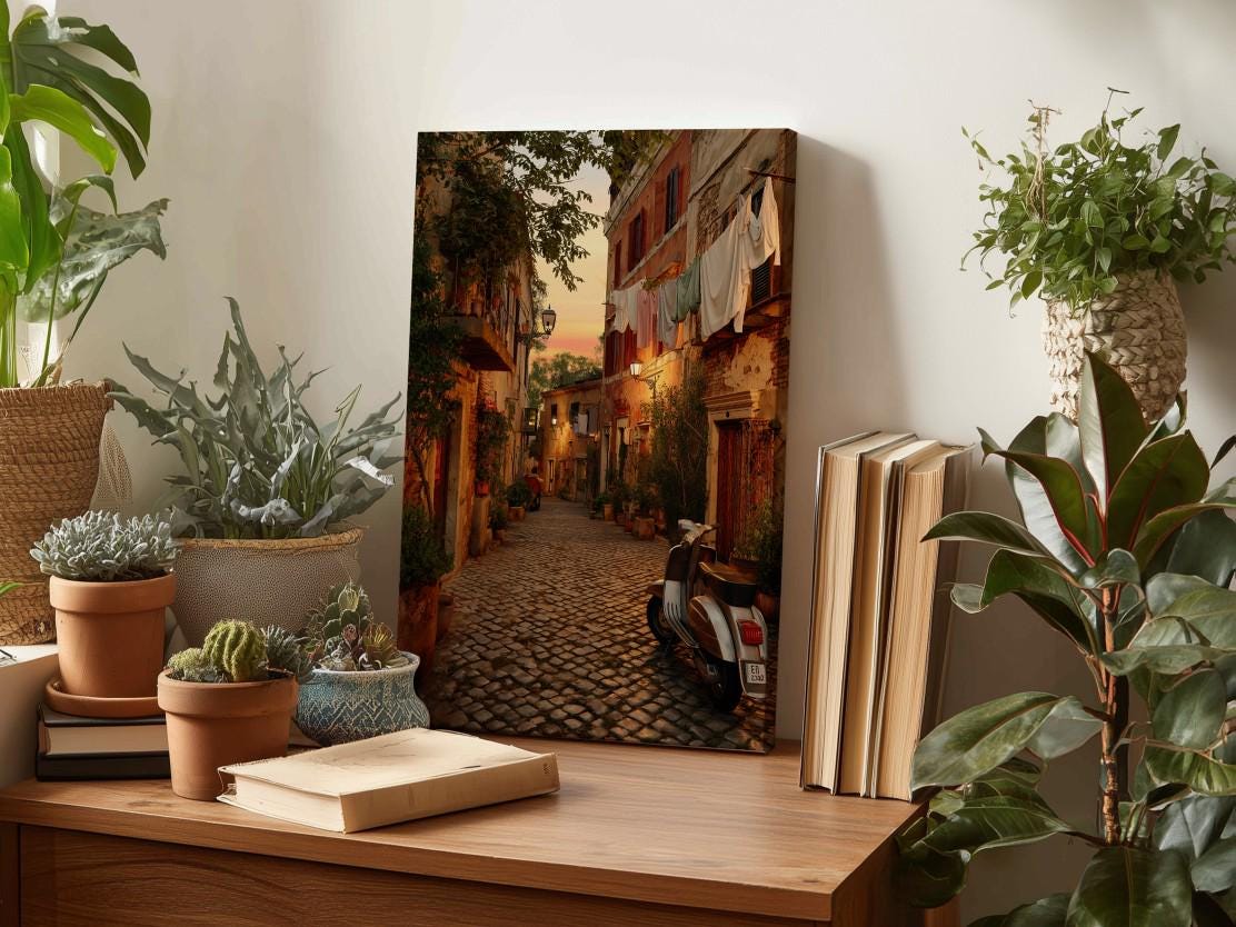 a cozy indoor setting with a wooden table displaying various items, including a framed photograph of a cobblestone street, potted plants, books, and a motorcycle.