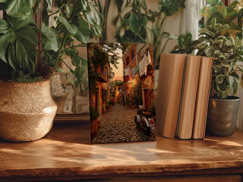 a wooden table with a framed photograph of a cobblestone street in a European village, surrounded by potted plants and books.
