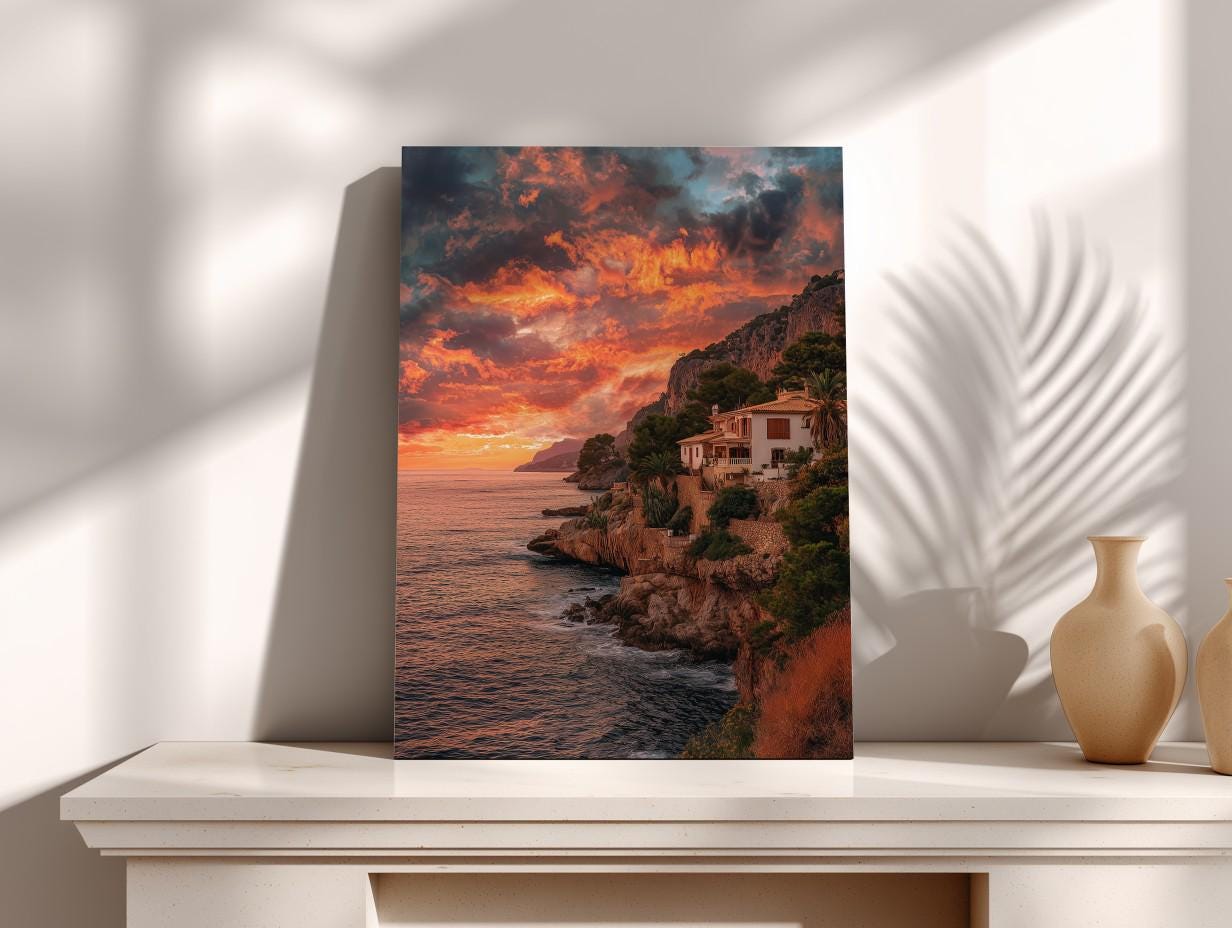 a coastal landscape with a house perched on a cliff overlooking the ocean. The sky is filled with vibrant colors, suggesting a stunning sunset or sunrise. The photograph is framed and displayed on a shelf, with two vases placed next to it.