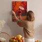 A woman hangs a vibrant painting of a woman in a red kimono on a wall, surrounded by a cozy indoor setting with a table of fruit and flowers.