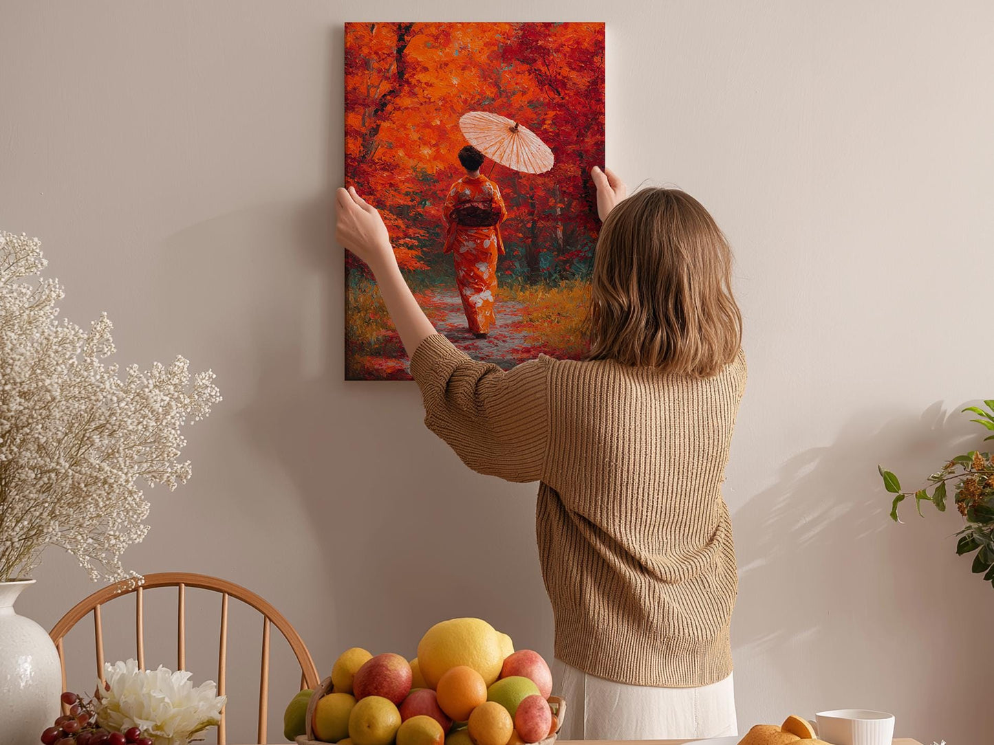 A woman hangs a vibrant painting of a woman in a red kimono on a wall, surrounded by a cozy indoor setting with a table of fruit and flowers.