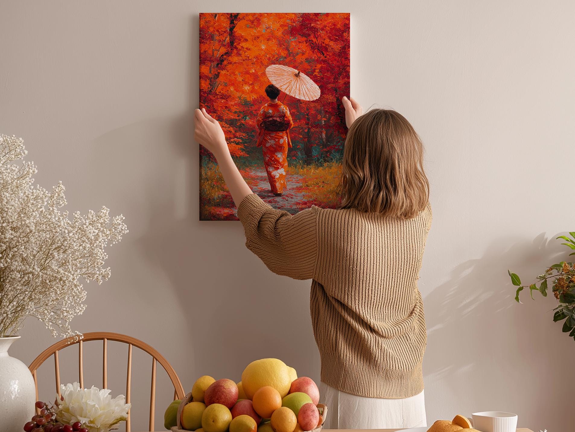A woman hangs a vibrant painting of a woman in a red kimono on a wall, surrounded by a cozy indoor setting with a table of fruit and flowers.