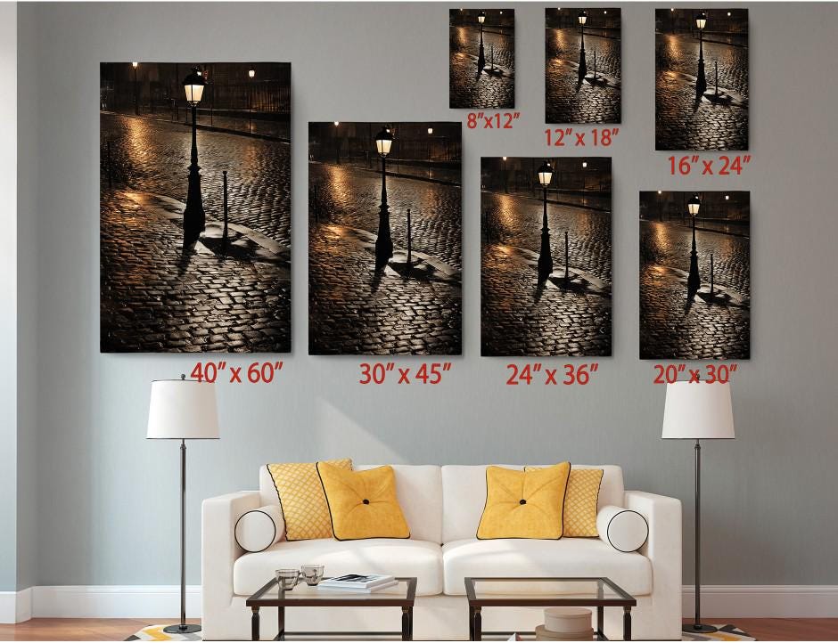 a living room with a white sofa and a coffee table, along with a lamp and a lamp post. Above the sofa, there are six framed photographs of street lamps and cobblestone streets, each with a different size and orientation. The photographs are arranged in a grid-like pattern on the wall, with each one having a corresponding size and orientation indicated below it.