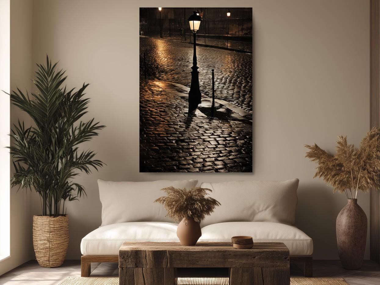 a serene indoor setting with a cozy couch, a wooden coffee table, and a potted plant. Above the couch, there is a large framed photograph of a street lamp and cobblestone pavement, creating a warm and inviting atmosphere.