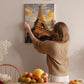 A woman hangs a framed picture of the Eiffel Tower on a wall in a room with a dining table, chairs, and various decorative items.