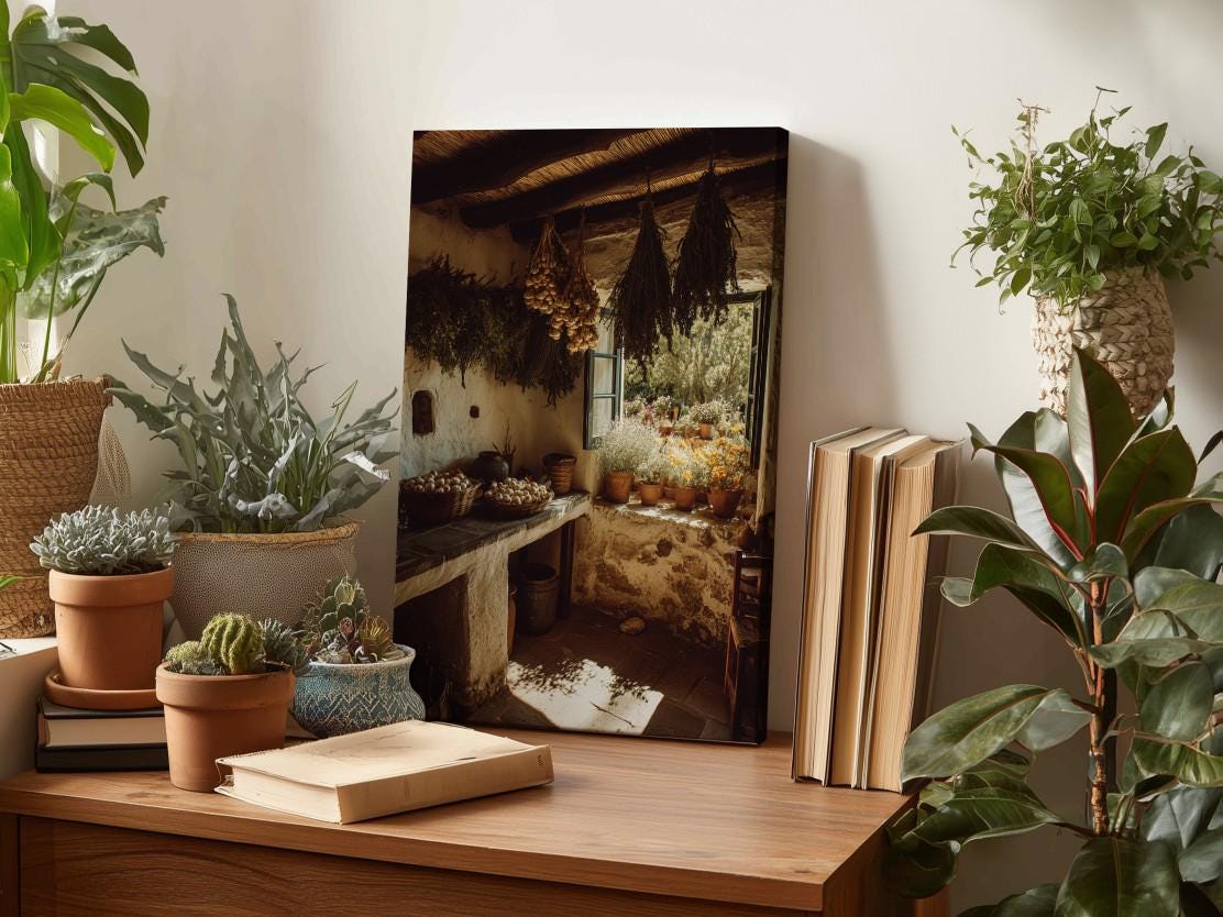 a wooden table with various potted plants, books, and a framed photograph of a rustic kitchen scene.