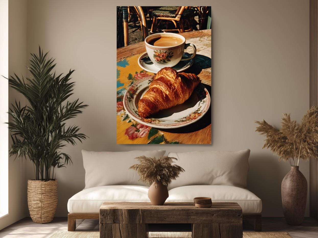 a cozy scene with a croissant on a plate, a cup of coffee, and a vase of dried flowers on a wooden table.