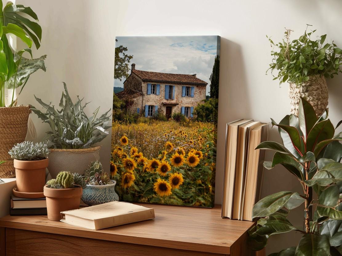 a wooden desk with a framed photograph of a house surrounded by a field of sunflowers, a potted cactus, and a stack of books.