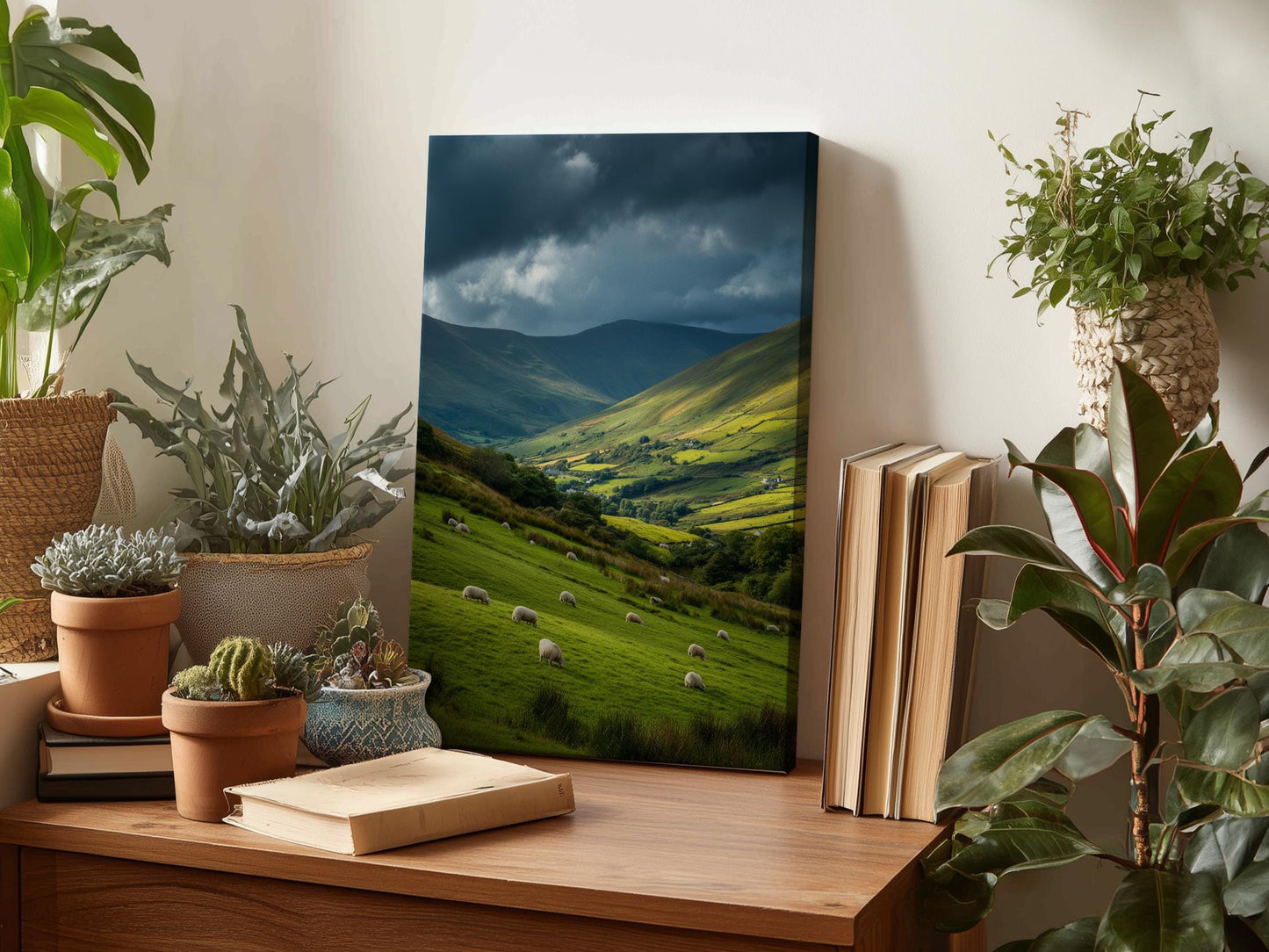 a wooden desk with a framed landscape painting depicting a pastoral scene with sheep grazing in a valley, surrounded by rolling hills and mountains. The painting is placed on a shelf, with several potted plants and books nearby, creating a cozy and natural atmosphere.