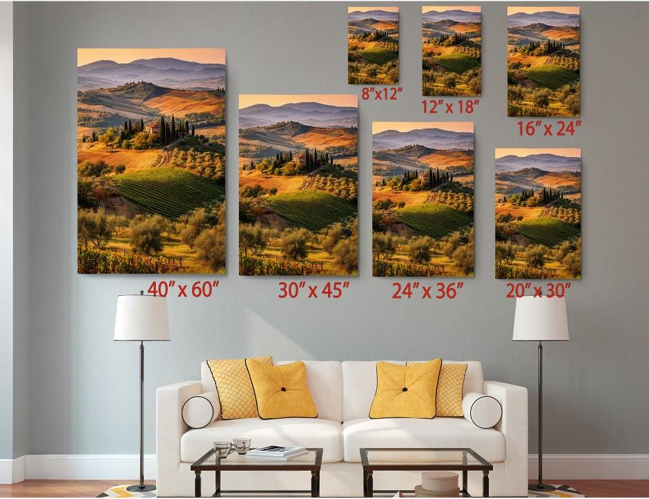 The image is a living room with a white sofa and a coffee table. Above the sofa, there are six framed landscape paintings of varying sizes, each depicting a different scenic countryside landscape. The paintings are arranged in a grid-like pattern, with each one showing a different perspective of the same landscape. The sizes of the paintings range from 6&quot;x12&quot; to 24&quot;x36&quot;, providing a diverse range of artistic representations of the picturesque countryside.