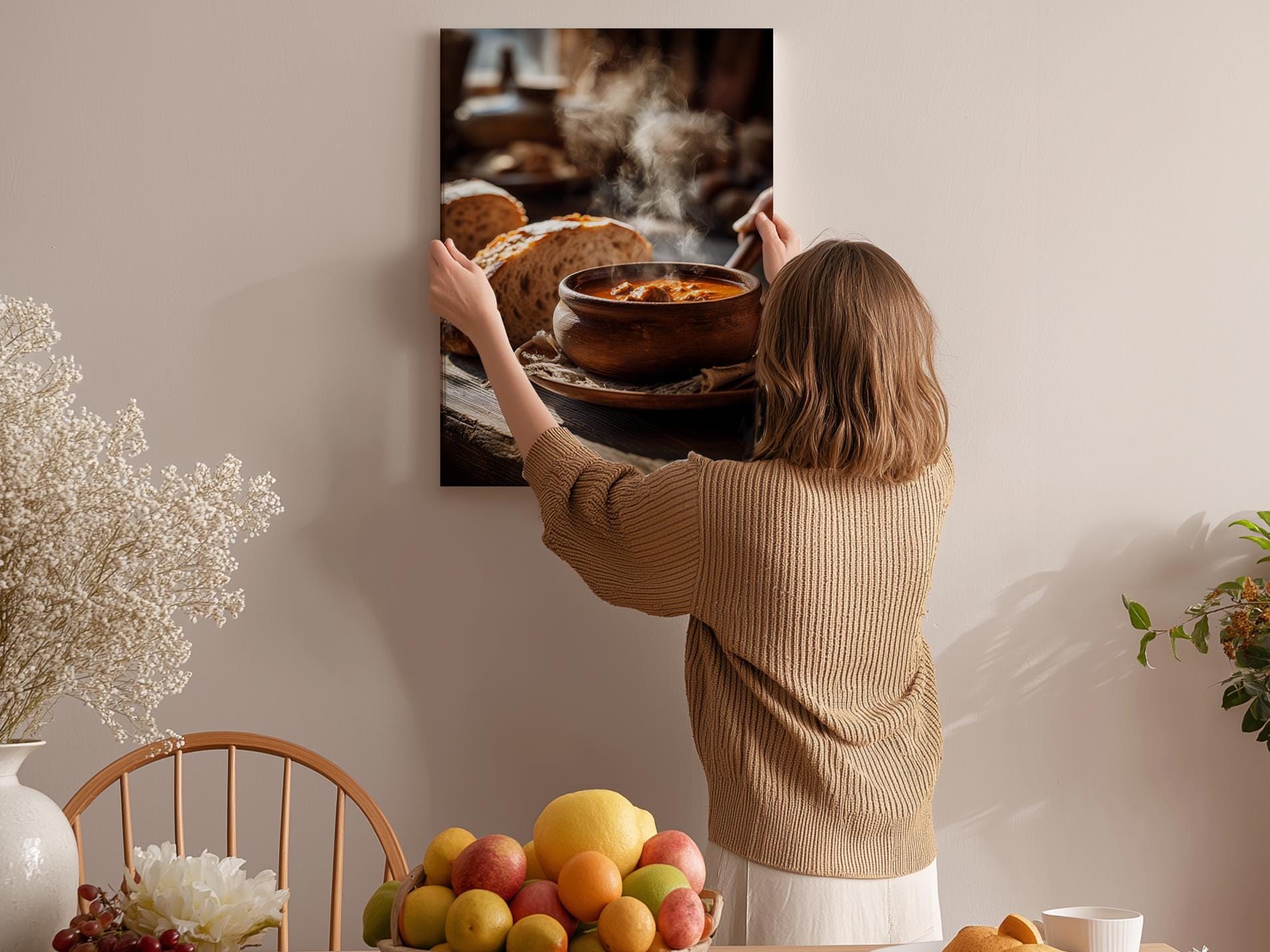 A woman hangs a framed photograph of a bowl of soup on a wall in a cozy kitchen setting.