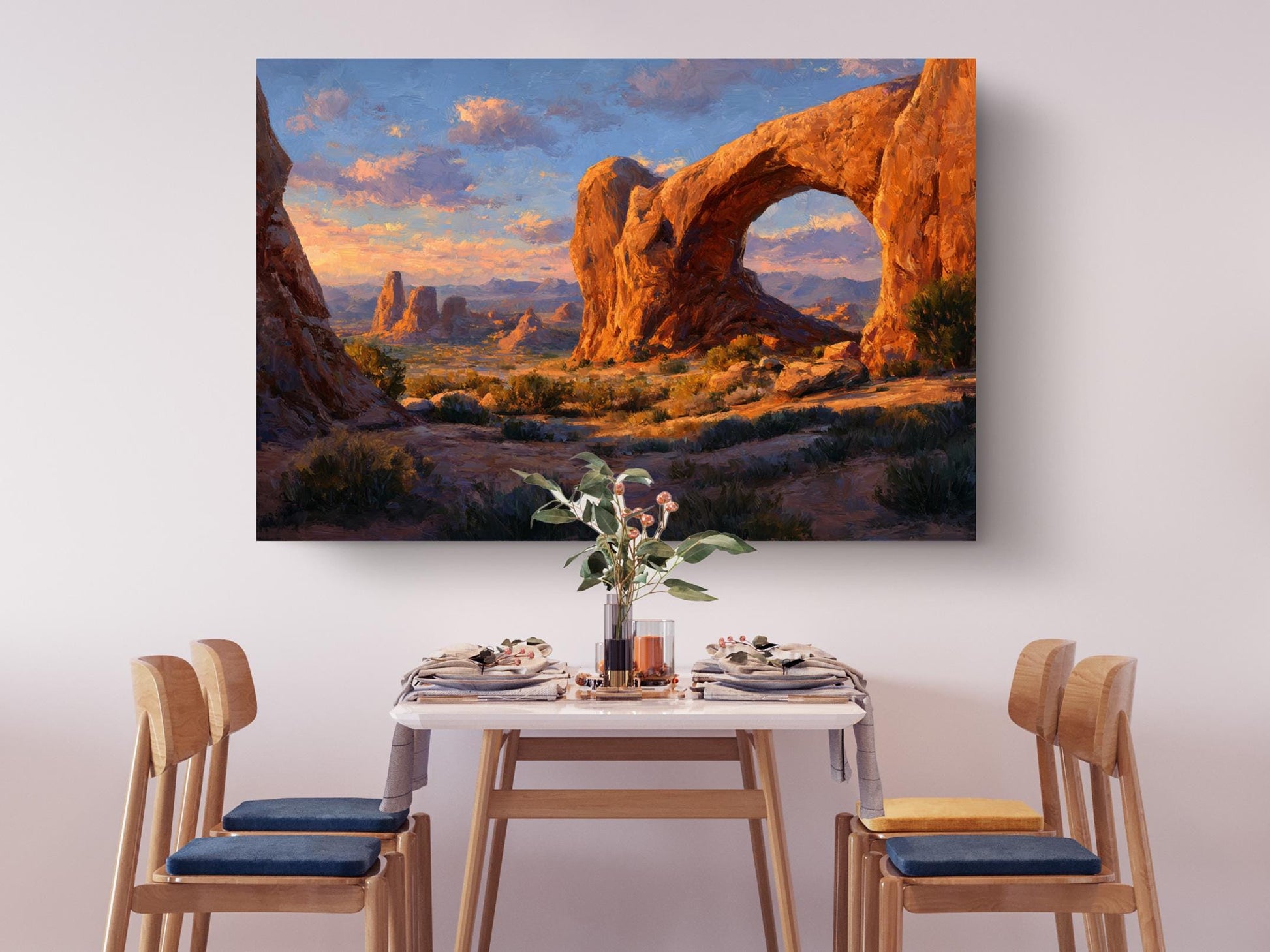 a dining table set with plates, silverware, and a vase of flowers, with a large painting of a desert landscape hanging above it.