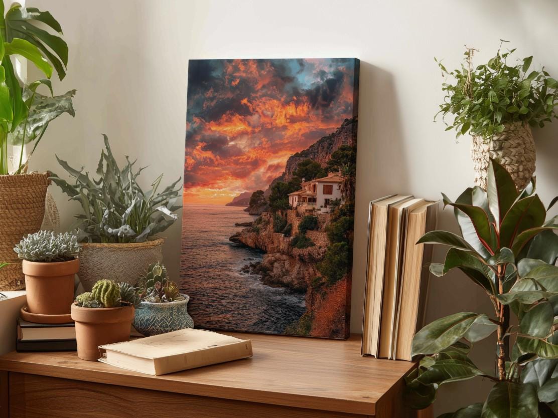 a wooden table with a framed photograph of a coastal cliff at sunset, surrounded by potted plants and books.