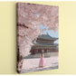 A woman in a pink dress stands in front of a traditional Korean temple, surrounded by cherry blossom trees in full bloom.