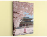 A woman in a pink dress stands in front of a traditional Korean temple, surrounded by cherry blossom trees in full bloom.