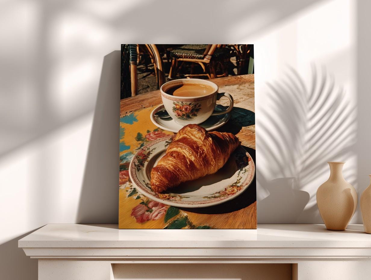 A croissant on a plate and a cup of coffee are displayed on a table, with a vase and a plant in the background.
