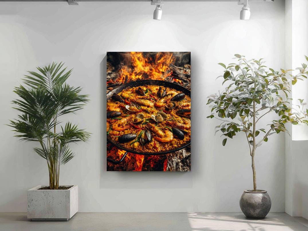 a large pan of seafood paella, with a fire underneath it, creating a dramatic effect. The pan is filled with various types of seafood, including shrimp, mussels, and clams, all cooked together in a traditional Spanish paella. The image is displayed on a wall, with a potted plant to the left and a plant to the right, adding a touch of greenery to the scene.