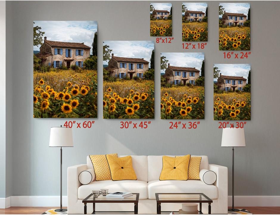 The image is a living room with a white sofa and a coffee table. Above the sofa, there are six framed prints of a house surrounded by a field of sunflowers, each with a different size and resolution. The prints are arranged in a grid pattern, with the largest print at the top and the smallest at the bottom. The prints are labeled with their respective sizes in inches, ranging from 40 to 36.