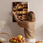 A woman hangs a framed photograph of cheese on a wall in a cozy kitchen setting.