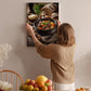A woman hangs a framed photograph of a hearty stew on a wall in a cozy kitchen setting.