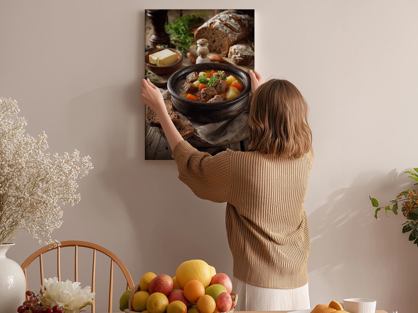 A woman hangs a framed photograph of a hearty stew on a wall in a cozy kitchen setting.