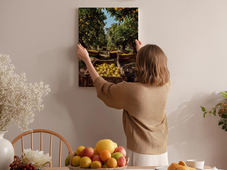 A woman hangs a framed picture of an orange grove on a wall in a room with a dining table, chairs, and various fruits.