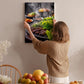 A woman hangs a framed photograph of a barbecue grill with various vegetables and meats on a wall in a cozy kitchen setting.