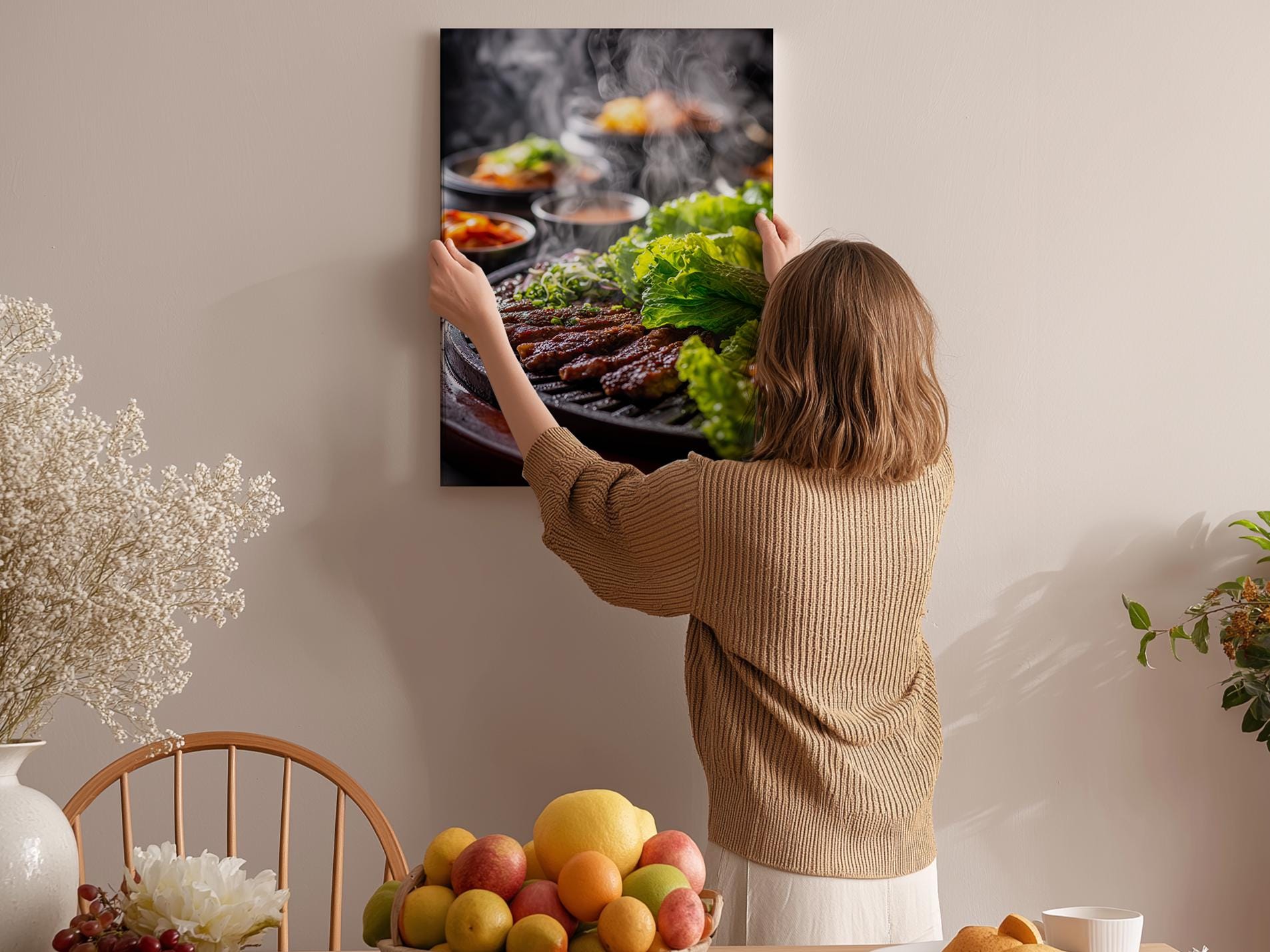 A woman hangs a framed photograph of a barbecue grill with various vegetables and meats on a wall in a cozy kitchen setting.