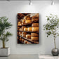 a wall with a large framed photograph of a wooden rack displaying various types of cheese. Next to the rack, there are two potted plants, one on each side of the frame.