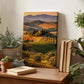 a wooden desk with a framed landscape painting depicting a scenic countryside view, surrounded by potted plants and books.