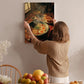 A woman hangs a framed picture of a meal on a wall, featuring a bowl of food and a plate of toast.