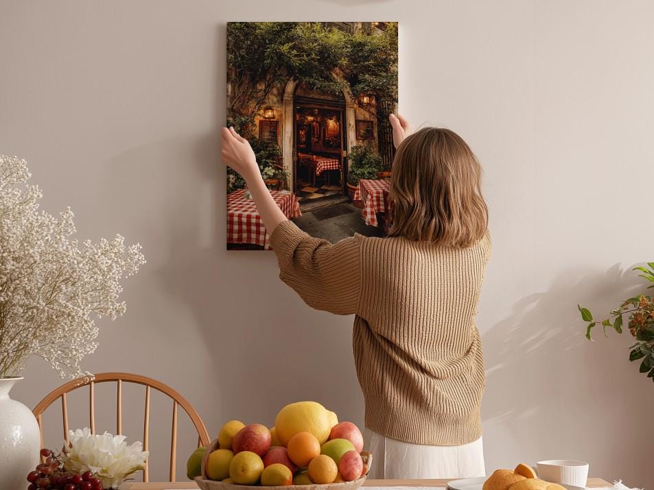 A woman hangs a framed picture of a restaurant on a wall in a cozy, homely setting.